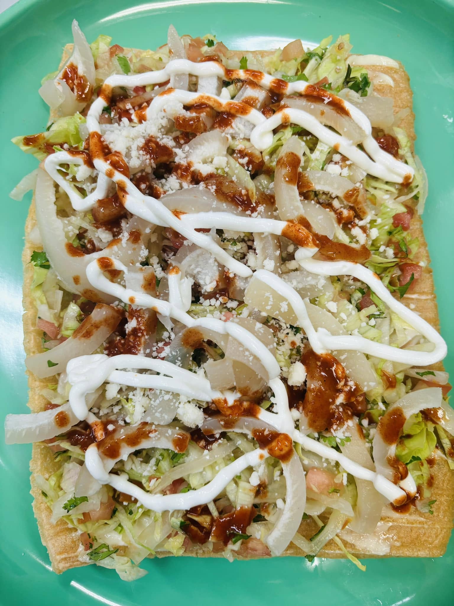 Tostada topped with meat, lettuce, crema and cheese
